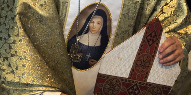 Ein Geistlicher trägt eine Kutte, eine Kreuzkette und ein Marienbild