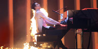 Ein Mann am Klavier, um ihn herum lodern Flammen