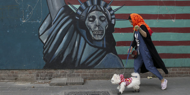 Eine Frau mit Hund geht an einem Grafitto einer Freiheitsstatue mit Totenkopf-Gesicht vorbei