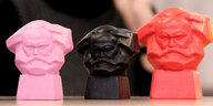 Drei kleine Pastiken in pink, schwarz und rot, die alle den Kopf von Karl Marx zeigen