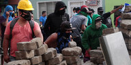 Vermummte Menschen hinter einem Wall aus Pflastersteinen