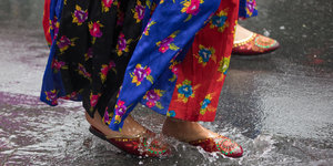 Teilnehmerinnen des Karneval der Kulturen in 2017 laufen in bunten Kostümen durch eine Regenpfütze