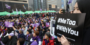 Eine Frau hält ein Schild, auf dem „#MeToo" und „#WithYou“ stehen