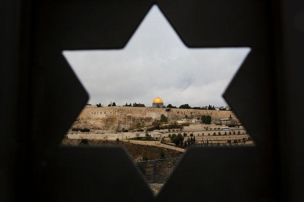 Blick durch einen sternförmigen Durchlass in einer Mauer, der die goldene Kuppel des Felsendoms umgeben von Häusern zeigt