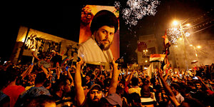 Eine Menschenmenge, in der ein Mann ein Porträgt von Muktada a-Sadr in die Höhe hält
