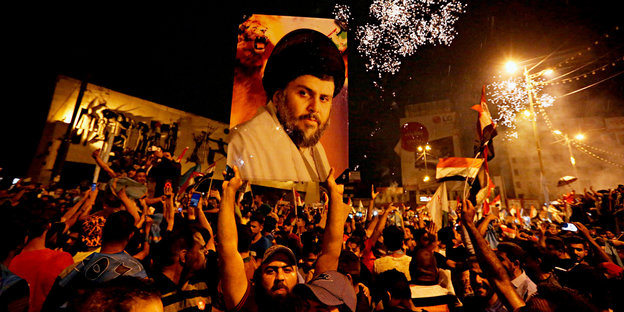 Eine Menschenmenge, in der ein Mann ein Porträgt von Muktada a-Sadr in die Höhe hält