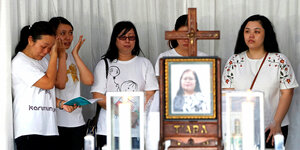 Mehrere Frauen in weißen T-Shirts stehen um ein Kreuz und trauern
