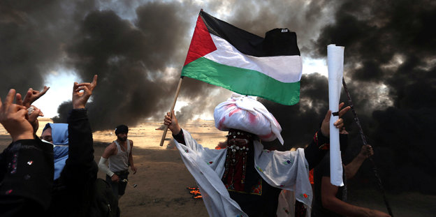 Inmitten von Rauchschwaden demonstriert eine Frau mit der palästinensischen Flagge