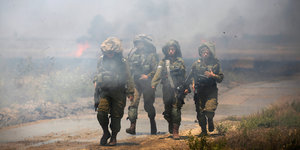 Vier Soldaten laufen durch eine Rauchwolke, hinter ihnen brennt es