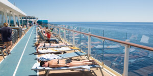 Auf dem Sonnendeck eines Kreuzfahrtschiffs liegen Menschen auf Liegen und sonnen sich.