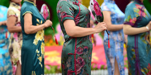 Sechs Frauen tragen verschiedenfarbige chinesische Seidenkleider und halten Fächer