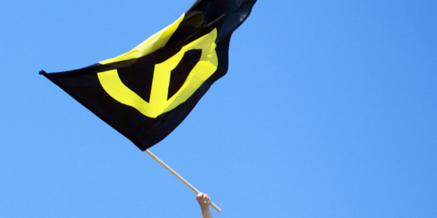 Eine Hand schwenkt eine Fahne mit dem Symbol der Identitären Bewegung