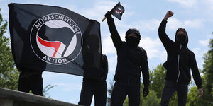 Schwarz gekleidete Menschen halten Flaggen der Antifa hoch