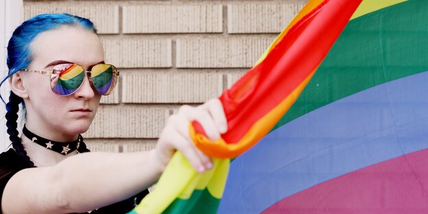 Eine Frau mit blauen Haaren hält energisch eine Regenbogenflagge