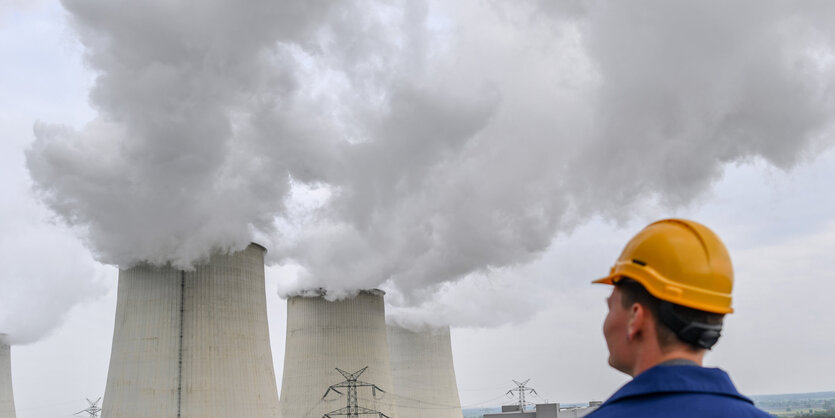 Ein Arbeiter schaut auf dampfende Kühltürme