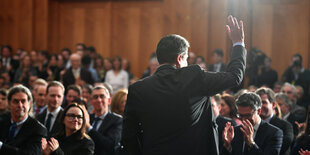 Sigmar Gabriel ist von hinten zu sehen, er steht im Scheinwerferlicht und hebtr die rechte Hand