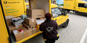 Eine Mitarbeiterin der Deutschen Post belädt einen Kleintransporter mit Paketen
