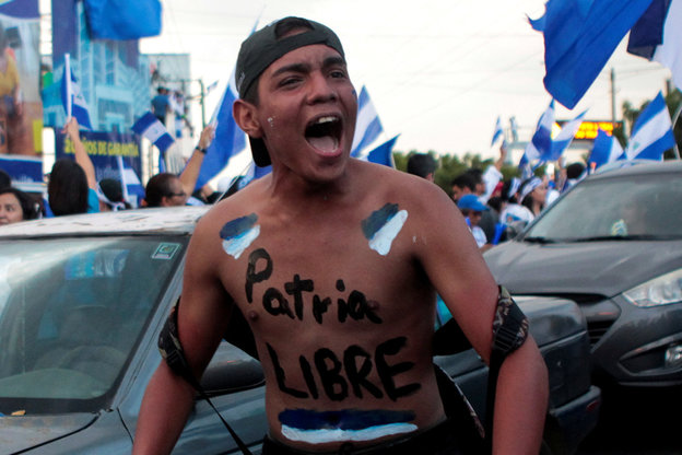 Ein Mann schreit bei einer Demonstration, auf seiner Brust steht "Patria Libre"