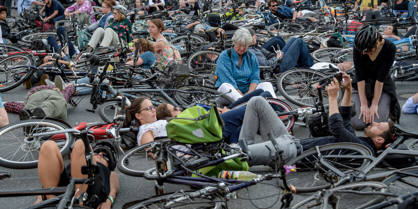 Radfahrer*innen sitzen und liegen auf einer Straßenkreuzung.