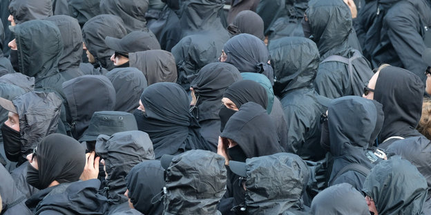 Eine große Gruppe von schwart gekleideten Menschen mit schwarzen Mützen und Sonnenbrillen