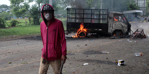 Ein maskierter Demonstrant läuft auf der Straße vor einem brennenden Lastwagen
