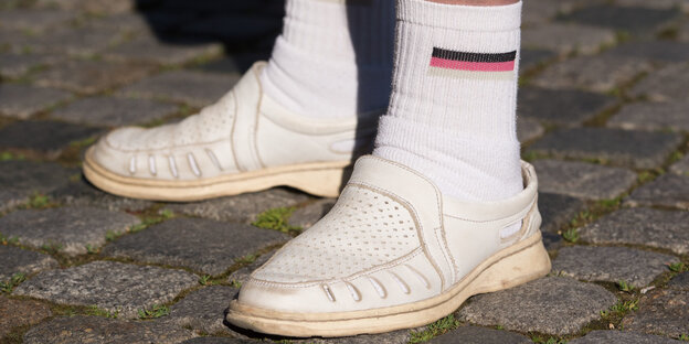 zwei Füße in weißen Lederschuhen mit knöchellangen Socken, die eine Deutschlandfahne ziert