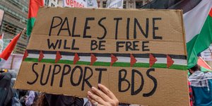 Eine Hand hält ein Schild auf dem Support BDS steht