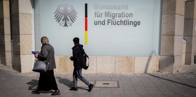 Eine Frau und ein Junge laufen am Logo des Bundesamtes für Migration und Flüchtlinge vorbei