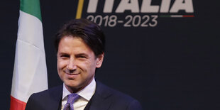 Giuseppe Conte steht vor einer italienischen Fahne und lächelt