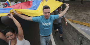 Ein Mann trägt eine rot-blau-gelbe Fahne hinter sich her