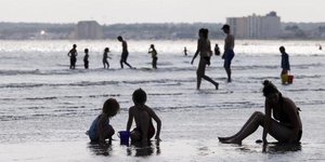 zwei Kinder und eine Frau sitzen am Strand