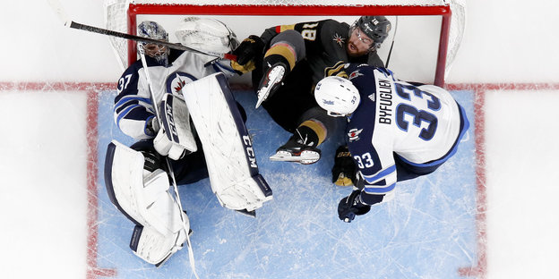 vor einem Eishockey-Tor liegen zwei Spieler auf dem Boden, einer steht daneben