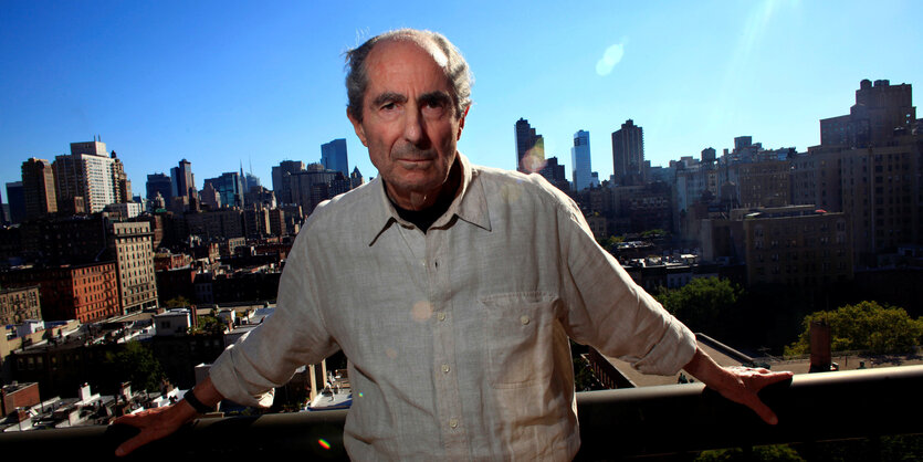 Philip Roth steht unter strahlend blauem Himmel vor der Skyline New Yorks