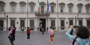 Touristinnen stehen auf einem Platz vor einem Gebäude und machen Fotos