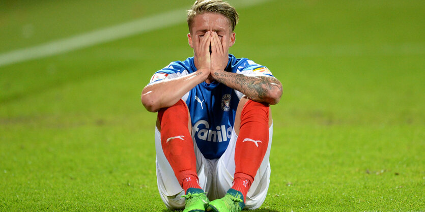 Der Kieler Fußballer Johannes van den Bergh sitzt am Boden und hält sich beide Hände vor das Gesicht.