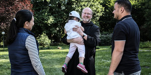 Ein Pfarrer hält ein Kind, zwei Erwachsene stehen daneben