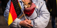 Eine Frau im Anorak hält eine Deutschlandflagge in der Hand und einen kleinen Hund auf dem Arm