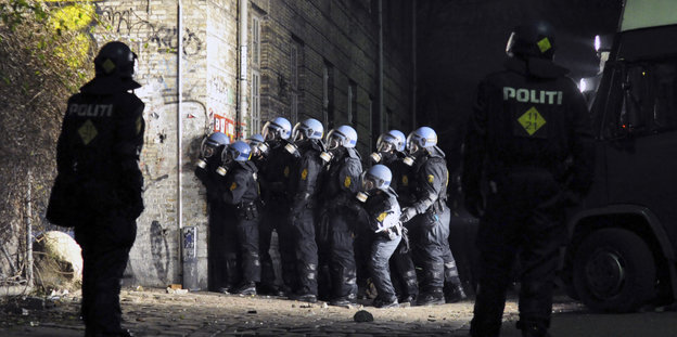 Polizisten in voller Montur stehen an einer Mauer