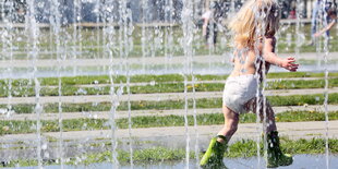 Ein Kind in einer Windel und mit Gummistiefeln rennt durch einen Springbrunnen