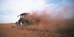 Ein Traktor fährt, eingehüllt in einer Staubwolke, über ein Feld