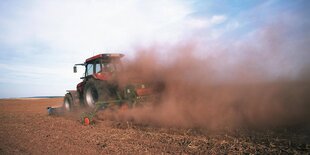 Ein Traktor fährt, eingehüllt in einer Staubwolke, über ein Feld