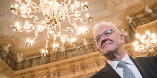 Winfried Kretschmann von unten aufgenommen - gegen die Decke eines Festsaals mit Kronleuchter