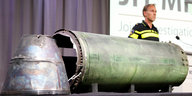 Auf einem Tisch werden Teile einer Rakete präsentiert, im Hintergrund ein Schild mit der Aufschrift MH17