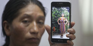 Eine Frau hält ein Smartphone mit einem Bild einer jungen Frau hoch.