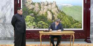 Vor einem großen Bild steht Kim Jong Un, an dem Tisch daneben sitzt Südkoreas Präsident und schreibt sich in das Gästebuch ein.