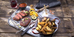 Ein Tablett auf einem Holztisch, darauf ein Steak, Pommes und andere Lebensmittel