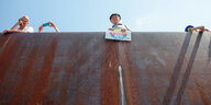 Von unten aufgenommen: Ufermauer an der Spree, über die verchiedene Leute schauen. Einer hält über die Mauer ein „Stoppt AfD“-Plakat