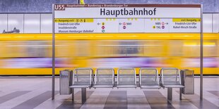 U-Bahnstation, im Mittelpunkt eine Sitzreihe, dahinter ein gelber U-Bahnzug, der schnell ein- oder abfährt