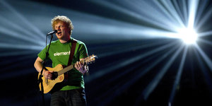 Ed Sheeran steht mit Gitarre auf der Bühne und singt