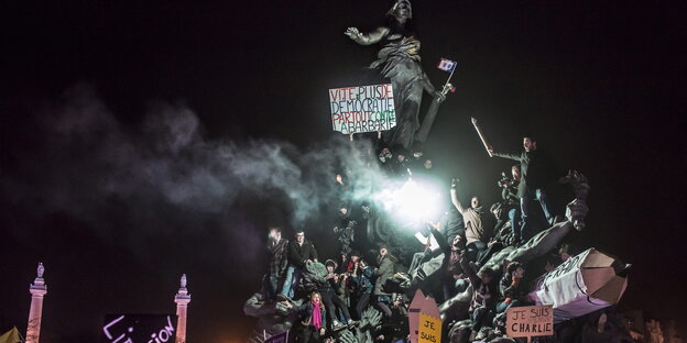 Menschen demonstrieren mit Plakaten auf einer Statue in Paris gegen die Anschläge im Jahr 2015